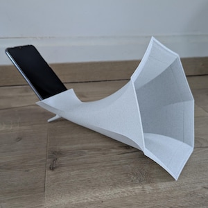 Könnte beinhalten: Ein weißes, papierartiges, 3D-gedrucktes Objekt in Form eines Megaphons, in dessen Öffnung ein Smartphone platziert ist.