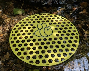 Schwimmender Tränkebehälter für Bienen, Hummeln, Schmetterlinge und Libellen in Form einer Honigwabe, der als ökologisches Wasserspiel auf dem Wasser platziert werden kann.
