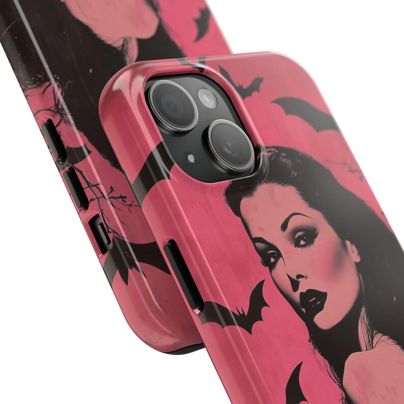 May include: Pink phone case featuring a woman's portrait with dark makeup and long black hair, along with black bat silhouettes. The case has a glossy finish and a camera cutout.