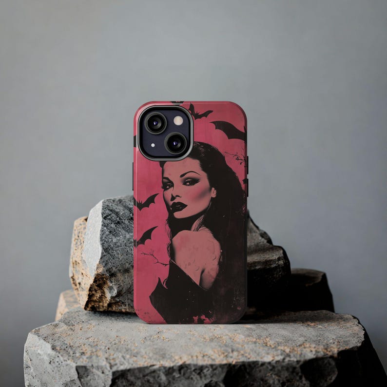May include: A phone case featuring a vintage-style illustration of a woman with dark hair and red lipstick, set against a pink background with bat silhouettes. The case is black and pink.