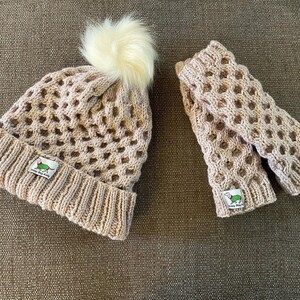 May include: A beige knitted hat with a white pom pom and matching fingerless gloves. Both items feature a green and white dachshund logo with the text "Happy Dog Co."