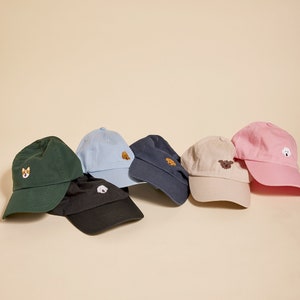 May include: Six different colored baseball caps with embroidered dog images. The caps are in a row, with the blue cap on the left and the pink cap on the right.