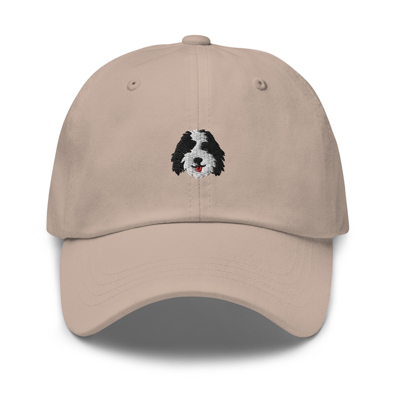 K&ouml;nnte beinhalten: Eine beige Baseballkappe mit einem gestickten schwarzen und wei&szlig;en Hundefoto auf der Vorderseite.