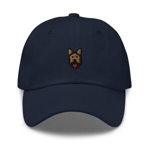 May include: A navy blue baseball cap with an embroidered brown and black German Shepherd dog face with a red tongue.