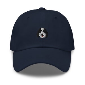 K&ouml;nnte beinhalten: Eine marineblaue Baseballkappe mit einem gestickten Bild eines schwarz-wei&szlig;en Hundes mit roter Zunge.