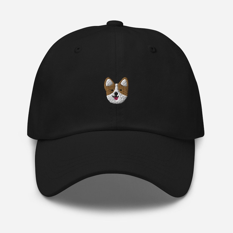 K&ouml;nnte beinhalten: Eine schwarze Baseballkappe mit einem gestickten Bild eines braunen und wei&szlig;en Hundes mit herausgestreckter rosa Zunge.