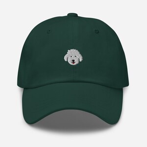May include: A dark green baseball cap with an embroidered white poodle face on the front.