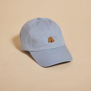 May include: A light blue baseball cap with a brown embroidered dog face on the front.