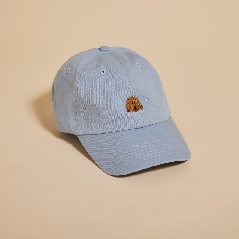May include: A light blue baseball cap with a brown embroidered dog face on the front.