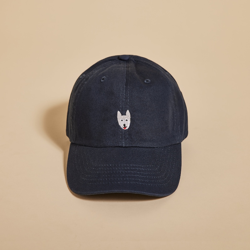 May include: A navy blue baseball cap with an embroidered white dog face on the front.
