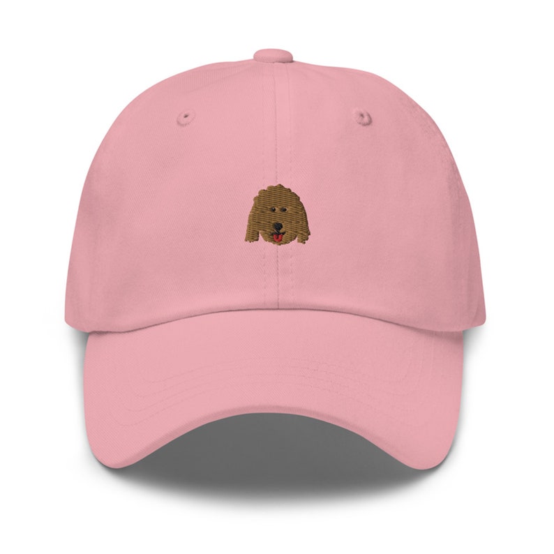 May include: A pink baseball cap with an embroidered brown dog face on the front.