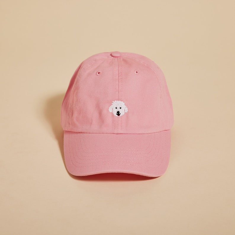 May include: A pink baseball cap with a white embroidered dog face on the front.