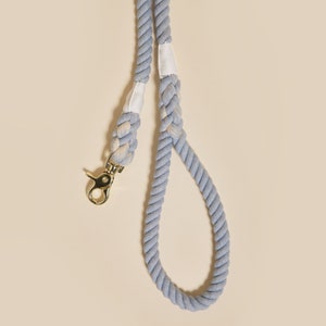 May include: A light blue cotton rope dog leash with a gold metal clip. The leash has white stitching and is braided.