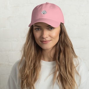 May include: A pink baseball cap with an embroidered white poodle on the front.