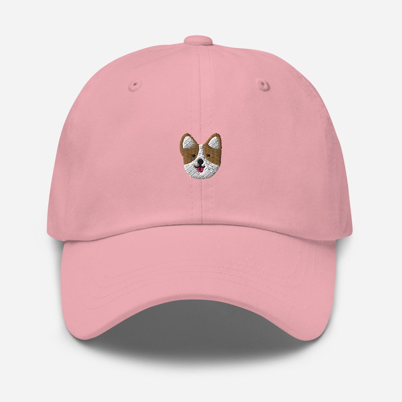 K&ouml;nnte beinhalten: Eine rosafarbene Baseballkappe mit einem gestickten Bild eines braunen und wei&szlig;en Hundes mit einer rosa Zunge.