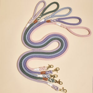 May include: Five colorful cotton rope dog leashes with gold metal clips. The leashes are arranged in a rainbow pattern with shades of pink, purple, and green.