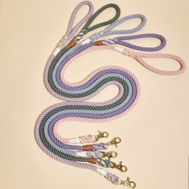 May include: Five colorful cotton rope dog leashes with gold metal clips. The leashes are arranged in a rainbow pattern with shades of pink, purple, and green.