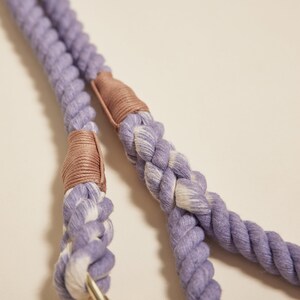 May include: A close-up of a purple and white rope dog leash with brown leather accents. The leash is made of a thick, braided rope and has a sturdy construction.