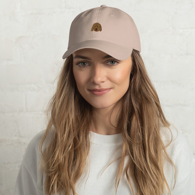 May include: A beige baseball cap with an embroidered brown dog face on the front.