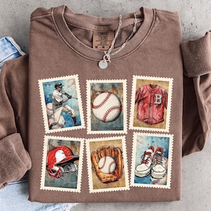 Puede incluir: Una sudadera marrón de manga larga con diseños de sellos postales con temática de béisbol. Los sellos representan un jugador de béisbol, una pelota de béisbol, una camiseta, un casco, un guante y zapatillas. También se ve un collar plateado con un colgante redondo.