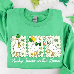 Peut inclure: Un sweat-shirt vert avec un motif de trois oies de dessin anim&eacute;, chacune avec des accessoires sur le th&egrave;me de la Saint-Patrick. Le texte "Lucky Goose on the Loose" est imprim&eacute; en dessous. Le sweat-shirt est en mati&egrave;re douce.