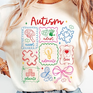 May include: Cream-colored t-shirt with the word "Autism" in red script. The shirt features colorful illustrations within decorative frames, including a brain, puzzle pieces, a handprint, a lightbulb, and a bow.
