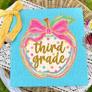 Pode incluir: Uma placa quadrada azul-clara com uma ilustração central de uma maçã com um laço rosa brilhante, texto em glitter dourado escrito third grade e bolinhas coloridas. Uma fita em forma de lápis com listras amarelas e brancas está presa no canto superior esquerdo.