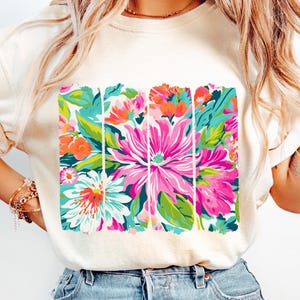 May include: A white t-shirt with a colorful floral print. The print features pink, green, blue, and orange flowers.
