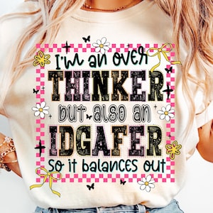 May include: Cream-colored t-shirt with a graphic design. The design features the text "I'm an over THINKER but also an IDGAFER So it balances out" in black, with pink and white accents, flowers, and butterflies.