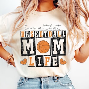 May include: A white t-shirt with the text "Livin' that Basketball Mom Life" in black and orange with a basketball graphic.