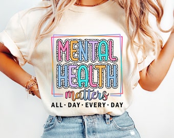 May include: A white t-shirt with a colorful graphic that says "Mental Health matters" in a box with a polka dot pattern. The text below the graphic says "All Day Every Day".