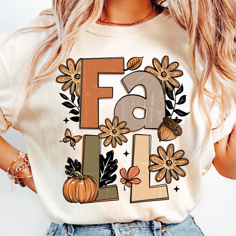 May include: Cream-colored t-shirt with the word "FALL" in brown, gray, and beige letters. The design includes fall-themed illustrations such as flowers, a pumpkin, an acorn, a butterfly, and leaves. The overall design has a vintage aesthetic.