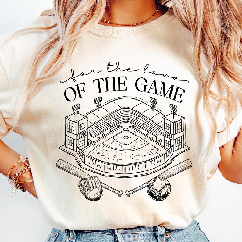 Op de afbeelding: Cr&egrave;mekleurig T-shirt met een zwart-witte honkbalstadionafbeelding en de tekst "for the love OF THE GAME". Het ontwerp bevat honkbalknuppels, een honkbal en een handschoen.