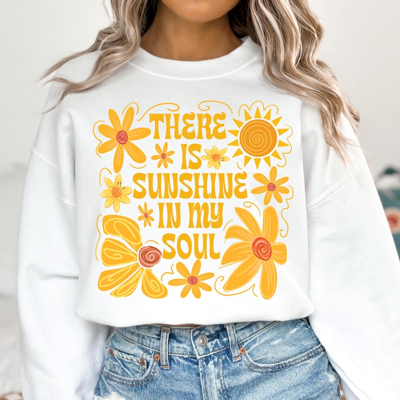 May include: White sweatshirt with a yellow and orange graphic design featuring flowers, a sun, and the text "There is sunshine in my soul."