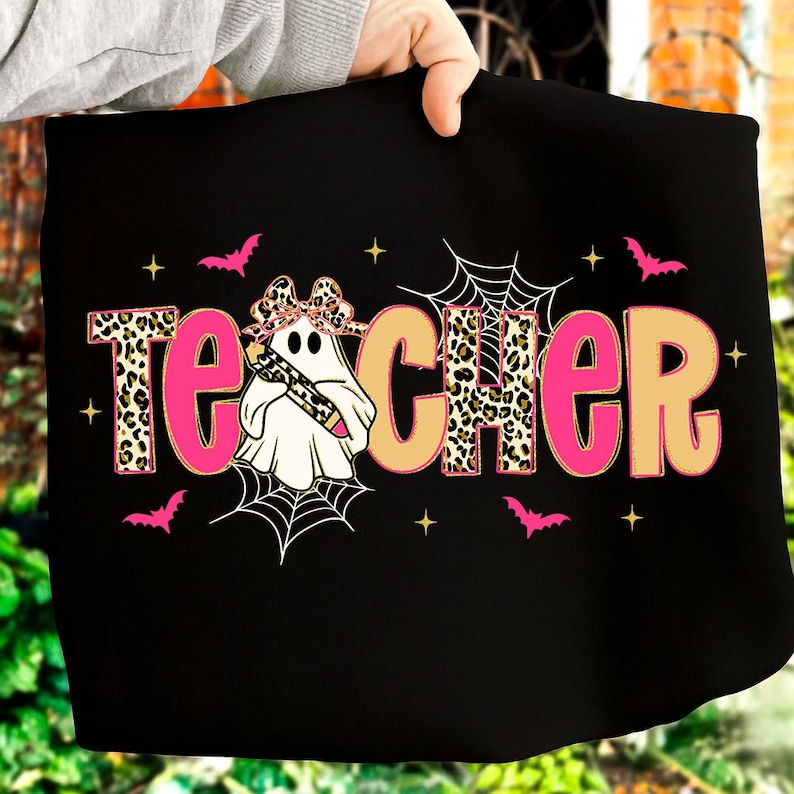 Pu&ograve; includere: T-shirt nero con la scritta "Teacher" in rosa e stampa leopardata beige. Un fantasma con un fiocco leopardato e una matita al centro. Pipistrelli rosa, ragnatele e stelle completano il design.