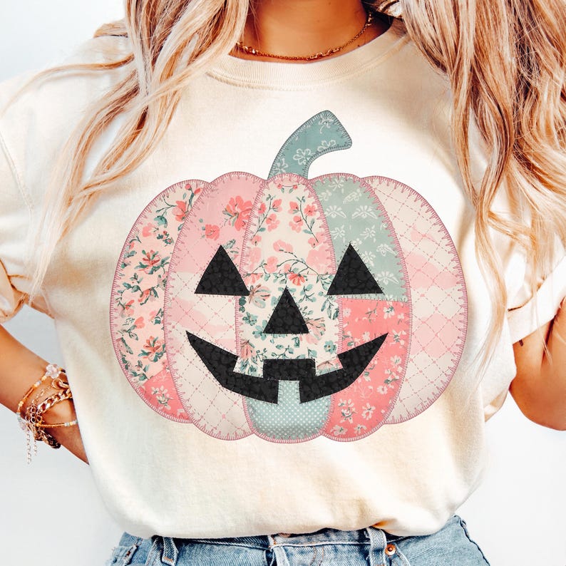 May include: A cream-colored sweatshirt featuring a patchwork pumpkin design. The pumpkin is made of floral and patterned fabrics in pink, green, and cream, with a black face. The design has a stitched appearance, perfect for fall and Halloween.