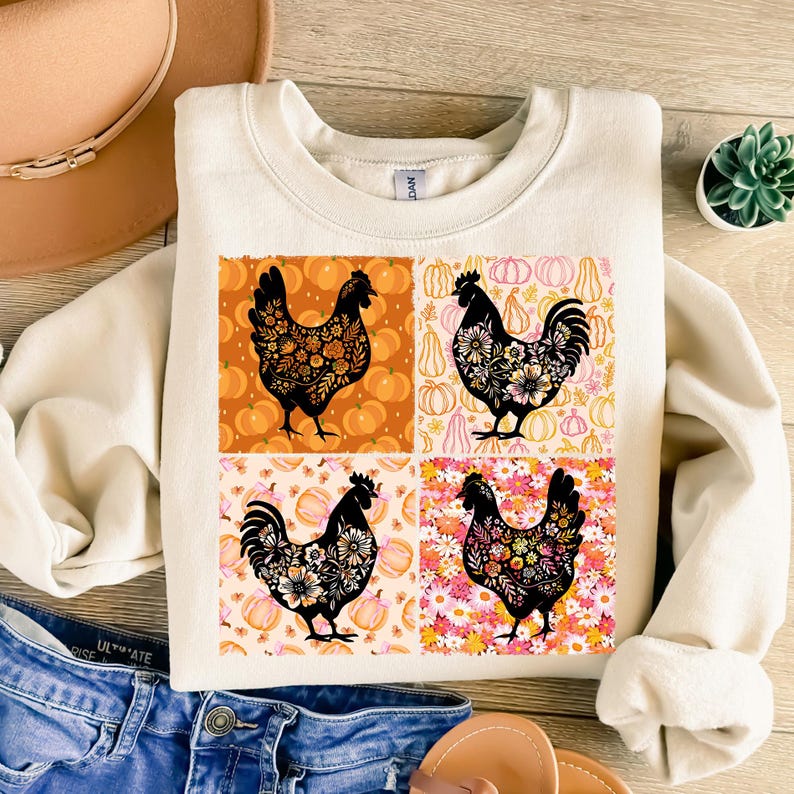 May include: Cream-colored sweatshirt featuring four square panels with black rooster silhouettes filled with floral patterns. Each panel has a different background of pumpkins and flowers in orange, pink, and white.