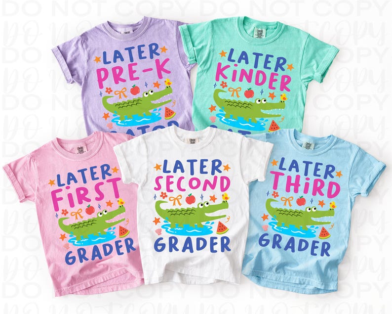 K&ouml;nnte beinhalten: Eine Auswahl an bunten T-Shirts f&uuml;r Kinder mit Schulmotiven. Jedes Shirt zeigt das Wort "Later" gefolgt von einer Klassenstufe, einem Cartoon-Alligator, einem Apfel und einer Wassermelone. Die Shirts sind in verschiedenen Farben erh&auml;ltlich, darunter Rosa, Blau und Wei&szlig;.