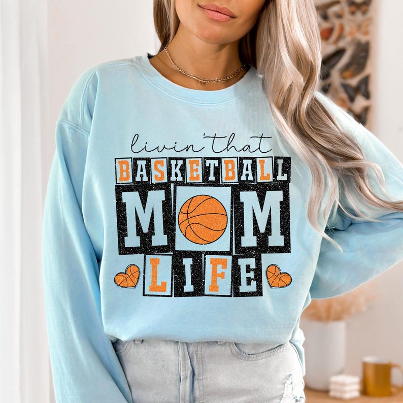 May include: Light blue sweatshirt with the text "Livin' that Basketball Mom Life" in black with a basketball graphic.