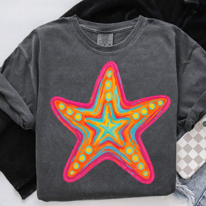 May include: Dark grey sweatshirt featuring a vibrant, hand-painted starfish design. The starfish is outlined in pink, with layers of orange, yellow, and blue. Yellow dots accent the starfish. The sweatshirt is made of a soft material.