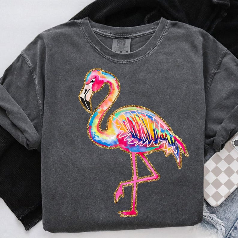 May include: A dark gray sweatshirt featuring a colorful flamingo design. The flamingo is depicted with vibrant rainbow hues, outlined in gold glitter. The sweatshirt has a crew neck and long sleeves, with a relaxed fit.