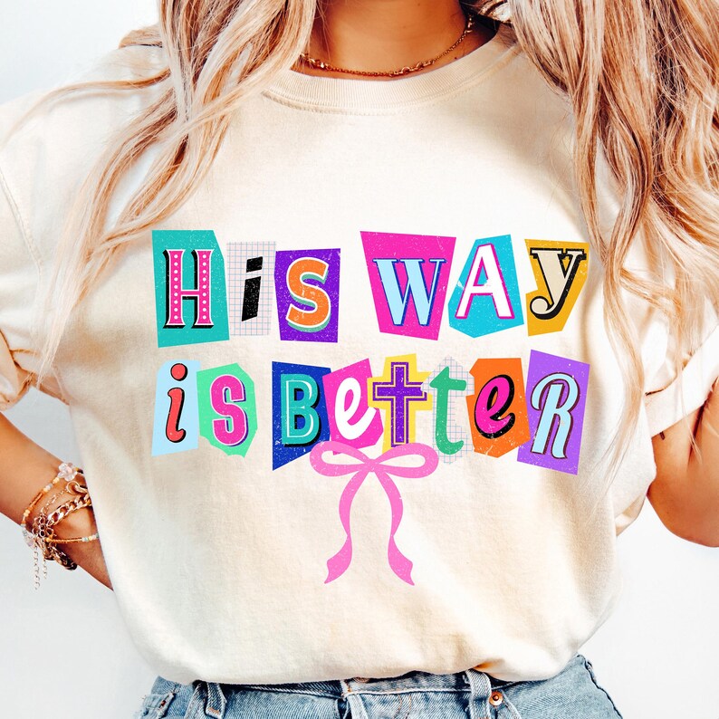 May include: Cream-colored sweatshirt with the text "His Way is Better" in colorful, cut-out style letters. A pink bow is below the text. The sweatshirt is a casual, comfortable style.