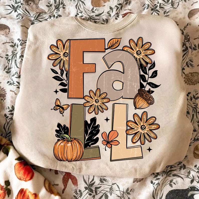 May include: Cream-colored sweatshirt with the word "FALL" in large, distressed letters. The design includes orange and tan flowers, a pumpkin, an acorn, a butterfly, and fall leaves. The sweatshirt has a crew neck.