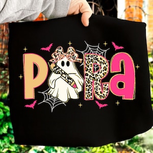 Pu&ograve; includere: T-shirt nero con la scritta "PARA" in beige, stampa leopardata e rosa. Un fantasma con un fiocco e una matita &egrave; al centro. Pipistrelli rosa e ragnatele decorano la maglietta, perfetta per Halloween.
