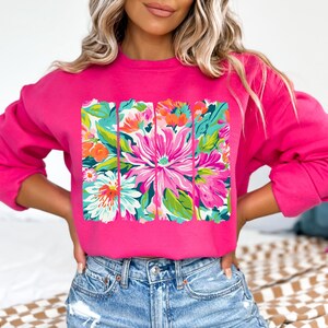 May include: A pink sweatshirt with a floral print design. The print features a variety of flowers in shades of pink, green, and white.