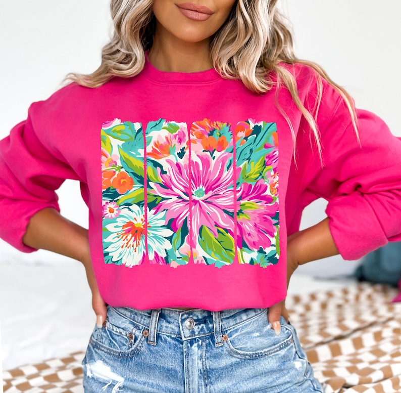May include: A pink sweatshirt with a floral print design. The print features a variety of flowers in shades of pink, green, and white.