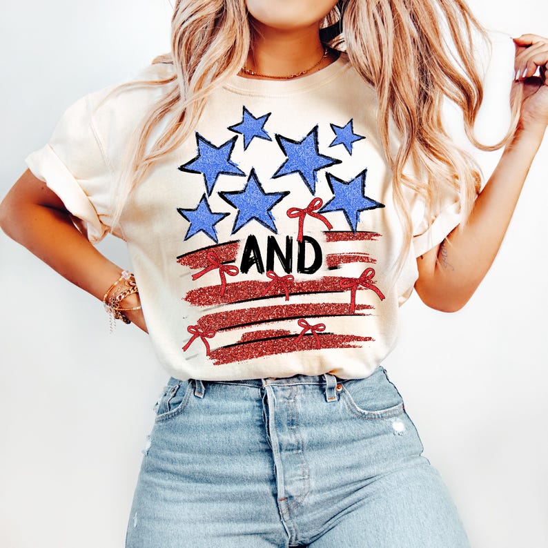 Pode incluir: Uma camiseta branca com um design de bandeira americana vermelha, branca e azul. A bandeira tem estrelas azuis e la&ccedil;os vermelhos. A palavra "AND" est&aacute; escrita em letras pretas na bandeira.