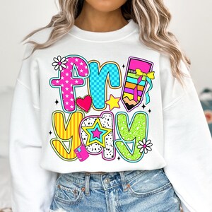 May include: White sweatshirt with a colorful graphic that says "friyay" with a pencil, stars, and hearts.