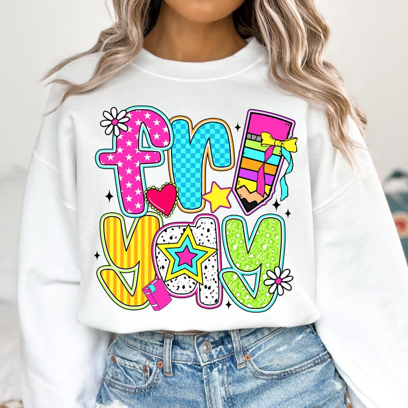 May include: White sweatshirt with a colorful graphic that says "friyay" with a pencil, stars, and hearts.