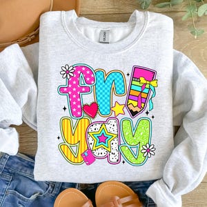 May include: A gray sweatshirt with a colorful graphic that says "Fri-yay" with a pencil, stars, and hearts.